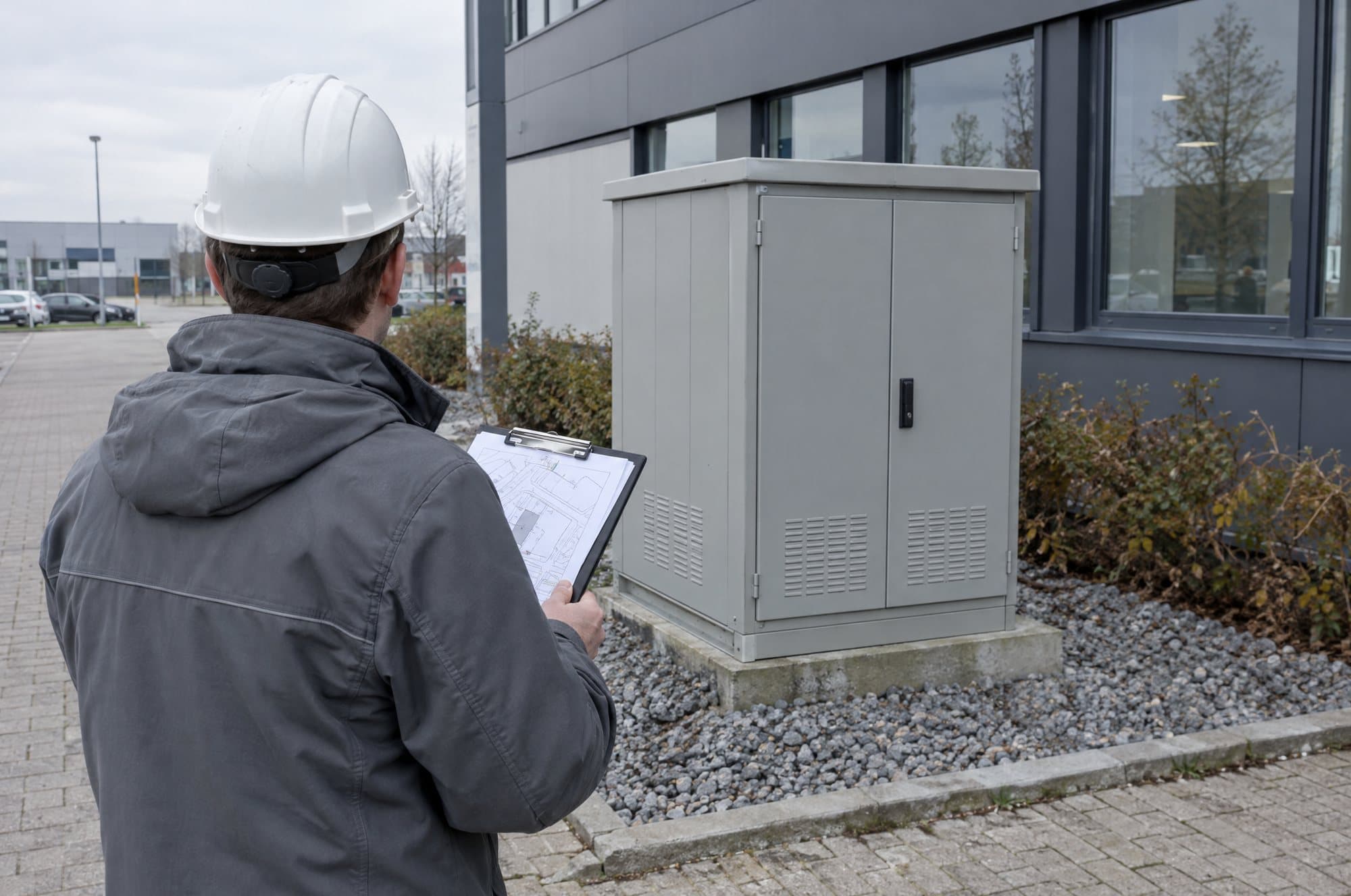 Ingenieur mit Standortplan vor einer Verteilung an einem Gewerbegebäude